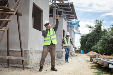 Asian construction project foreman with beard inspects construction site using technology tablet...