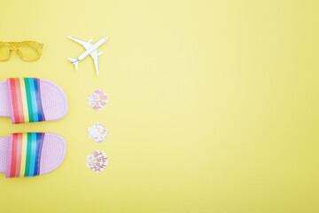 Rainbow slippers, toy airplane, seashells and sunglasses on a yellow background. Summer holiday, travel and vacation concept. Flat lay, copy space