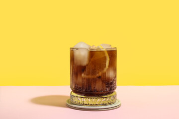 Glass of Long Island iced tea cocktail on pink table against yellow background