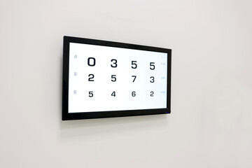 Electronic vision chart with large black numbers on a white background, displayed on a wall-mounted...