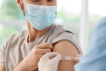 Young man with doctor applying medical patch after vaccination in clinic, closeup