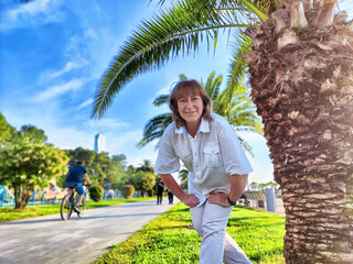Middle-aged blonde woman enjoying a sunny excursion in a palm-lined park while taking a selfie...
