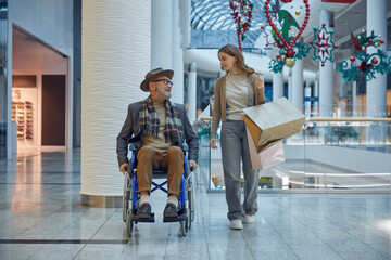 A man in a wheelchair is assisted by a woman in a mall