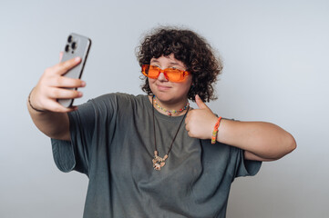 portrait of young surprised curly-haired woman enjoys taking selfies, showcasing their trendy...