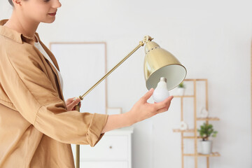 Young woman screwing light bulb into standard lamp at home