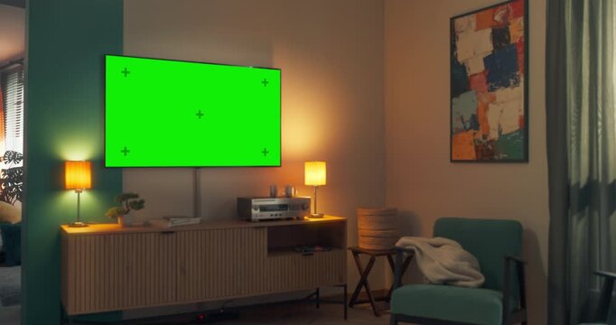 Television Set at Home with a Green Screen Chroma Key Template with Placeholders. TV Hanging on the Wall in a Bright Modern Apartment. Zoom Out to a Man Sitting on a Sofa and Watching TV