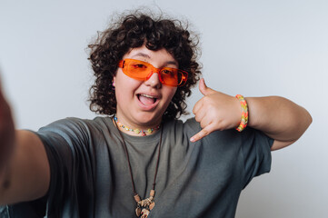 portrait of young surprised curly-haired woman poses for a selfie with a playful gesture on light...
