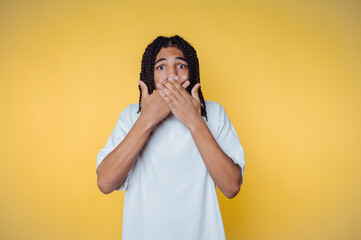 portrait of young man expresses surprise by covering his mouth on yellow background