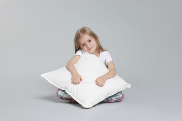 Cute little girl in pajamas with pillow on grey background