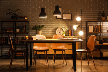 Interior of dark room with bookshelves, table and glowing lamps at night