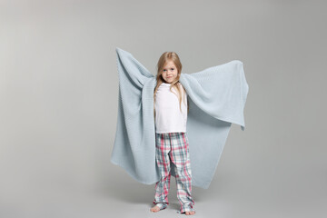 Cute little girl in pajamas with plaid on grey background