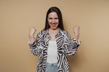 portrait of young woman cheers with her fists raised, embodying joy and triumph on calm yellow...