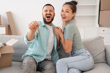 Young couple with key from their new house holding hands on sofa in room
