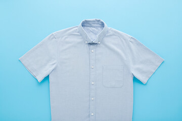 New clean classic shirt on light blue table background. Pastel color. Closeup. Male formal clothes. Top down view.