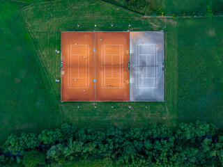Top view of tennis courts in rural setting with surrounding trees and clear field lines.