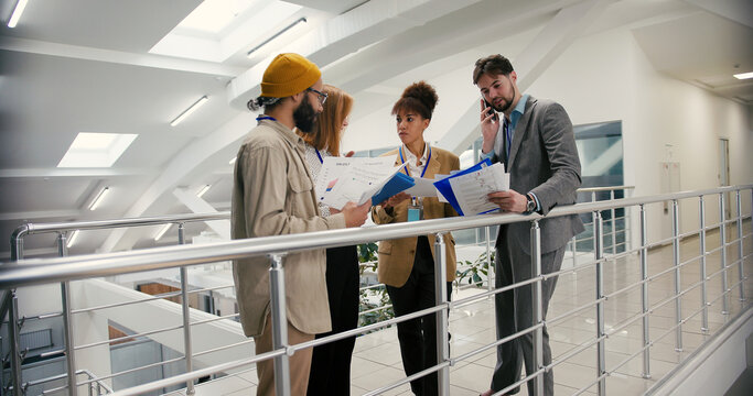 Diverse businesspeople review documents standing in corridor