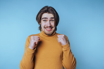 portrait of young man showcases pure joy and celebration while clenching his fists on blue...