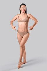 Young woman in underwear with cellulite problem pointing at her legs on grey background