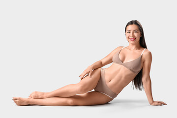 Fototapeta premium Young woman in underwear with cellulite problem lying on light background