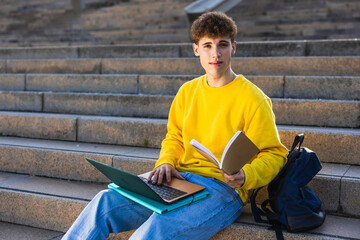 College student studying with laptop and book on stairs
