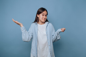 portrait of young woman looks confused with a humorous shrug on light blue background