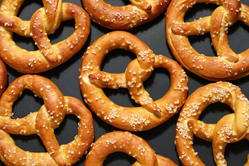 Many tasty salted pretzels on black background