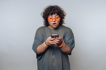 portrait of young surprised curly-haired woman with surprised expression looking at a smartphone on...