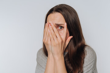 portrait of young fearful woman covers her face with her hands, showing vulnerability and internal...