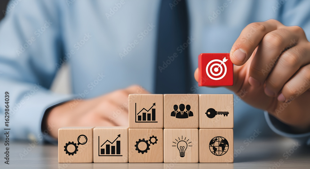 Poster hand placing red target block at top symbolizing achievement and goals on stack of wooden blocks wit