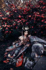 Naklejka premium Asian woman in ornate dress among blooming flowers.