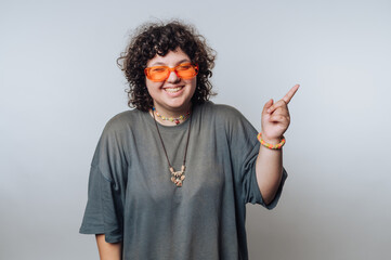 portrait of young surprised curly-haired woman smiling wide while wearing orange sunglasses,...