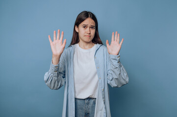 portrait of young young woman stands with her hands raised in concern on light blue background