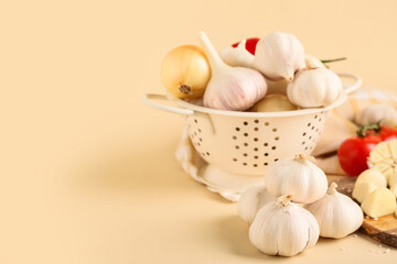 Colander with fresh garlics and onions on beige background