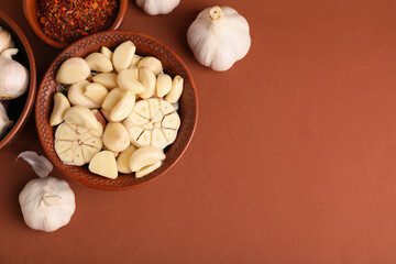 Bowl with fresh garlic cloves and spices on brown background