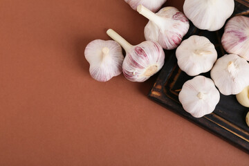 Wooden board with fresh garlics on brown background