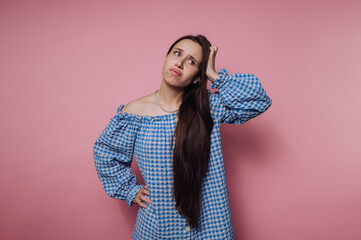 portrait of young woman with a puzzled expression scratches her head, wearing a blue checkered...