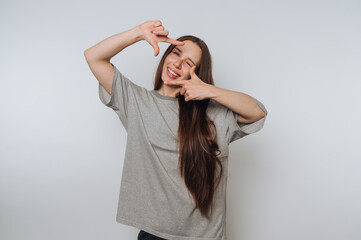 Fototapeta premium portrait of young joyful woman playfully frames a scene with her hands, showcasing creativity and a fun on light background