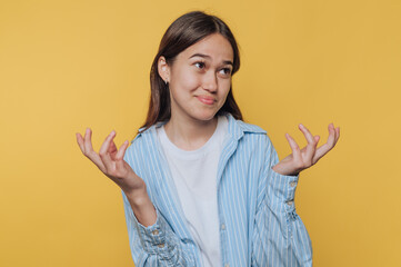 portrait of young woman displays confusion with a thoughtful expression while standing on yellow...