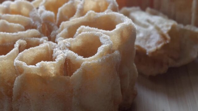 Zoom in on a flor frita, a Spanish sweet fried pastry with flower shape and sugar coating over wooden background.