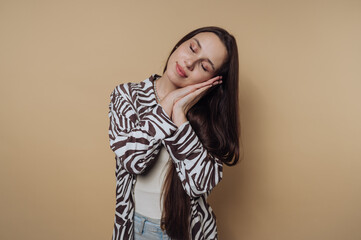 portrait of young woman in a zebra print shirt pretending to sleep with a serene expression on calm yellow background