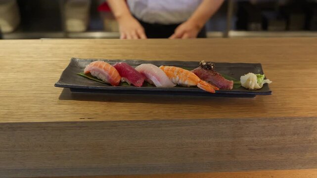 A sushi chef presents his beautifully plated fresh nigiri sushi with 5 different types and flavours with a side of pickled ginger.