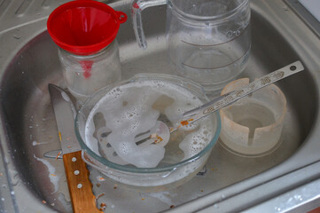 dirty dishes with soap suds and utensils in kitchen sink next to jug and funnel under metal faucet...