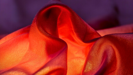 Close-up view of vibrant, flowing fabric with rich red and purple hues, showcasing texture and light.