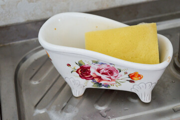 yellow sponge and decorative floral ceramic bowl placed on wet kitchen sink near faucet kitchen...