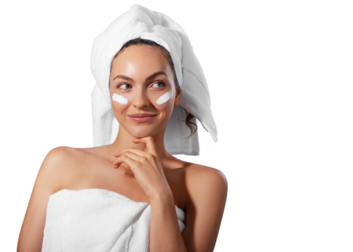 Smiling young woman applying facial cream under her eyes, wrapped in a white towel with a towel turban on her head. PNG with transparency