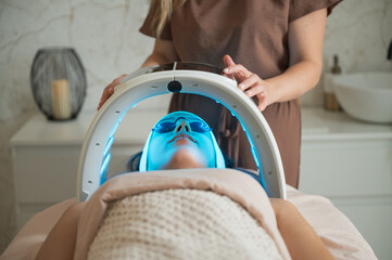 Woman receiving blue LED light therapy under dome device medium shot recognizable concept
