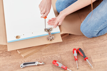 A woman is focused on assembling furniture using various tools on a wooden floor. She is applying a...