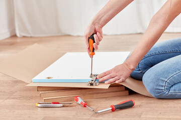 Individual works on assembling a piece of furniture with tools scattered nearby. The setting...
