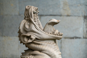 Massandra Palace of Emperor Alexander III. Close up detailed stone sculpture of mythical dragon, showcasing intricate carvings and fierce expression, set against weathered stone wall.