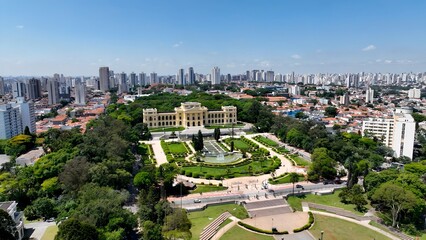 Independence Museum In Ipiranga Park Sao Paulo Brazil. Drone Captures A Garden With Sidewalks Surrounded By Lush Trees. Business Clouds Sky Downtown Cityscape. Backgrounds Panoramic.